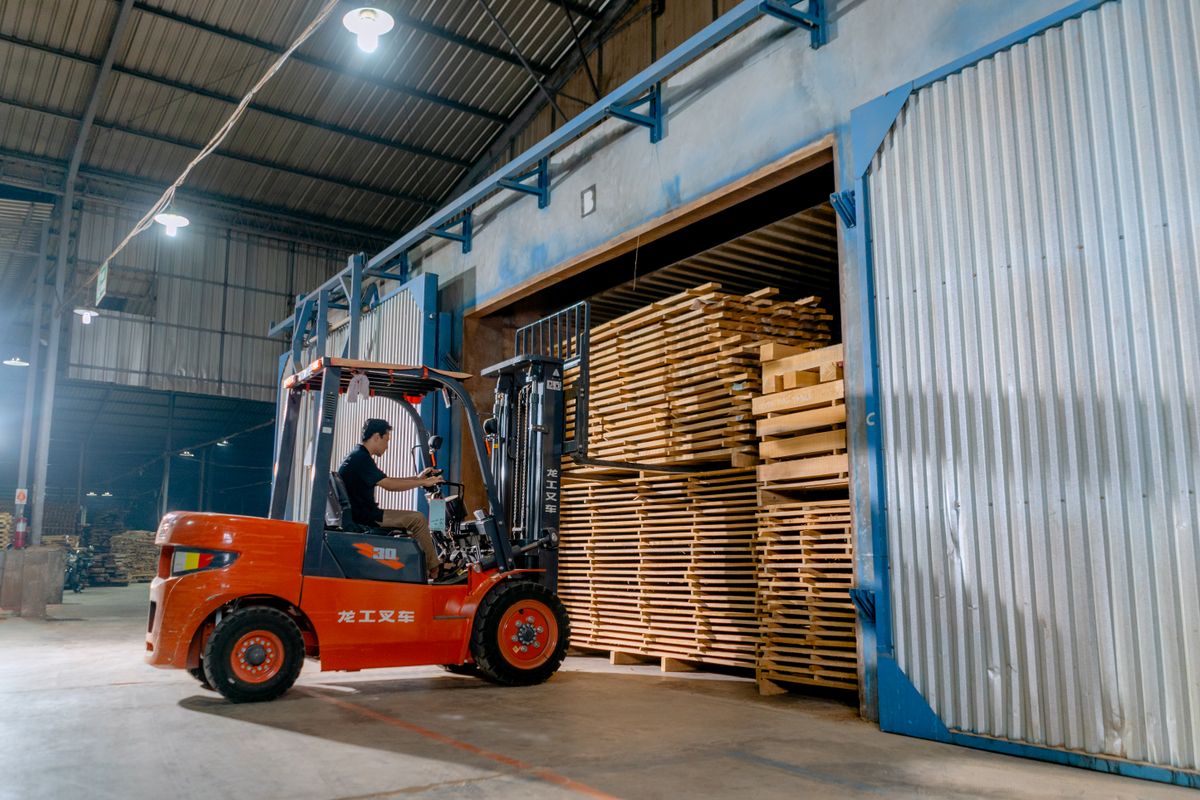 Forklift operator loading stacks of timber pallets at a warehouse door