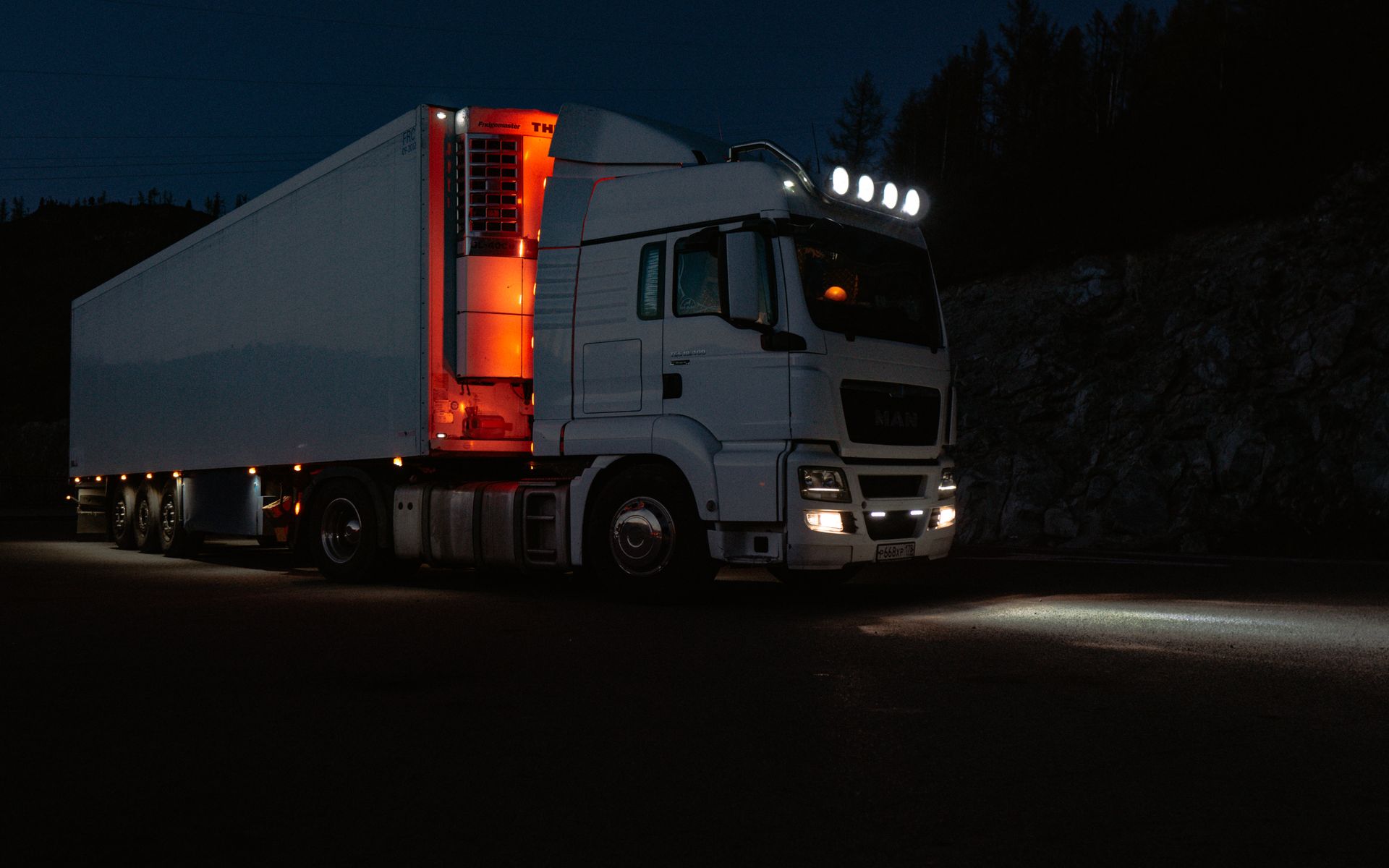 White articulated lorry with a refrigerated trailer parked at night with its running lights on