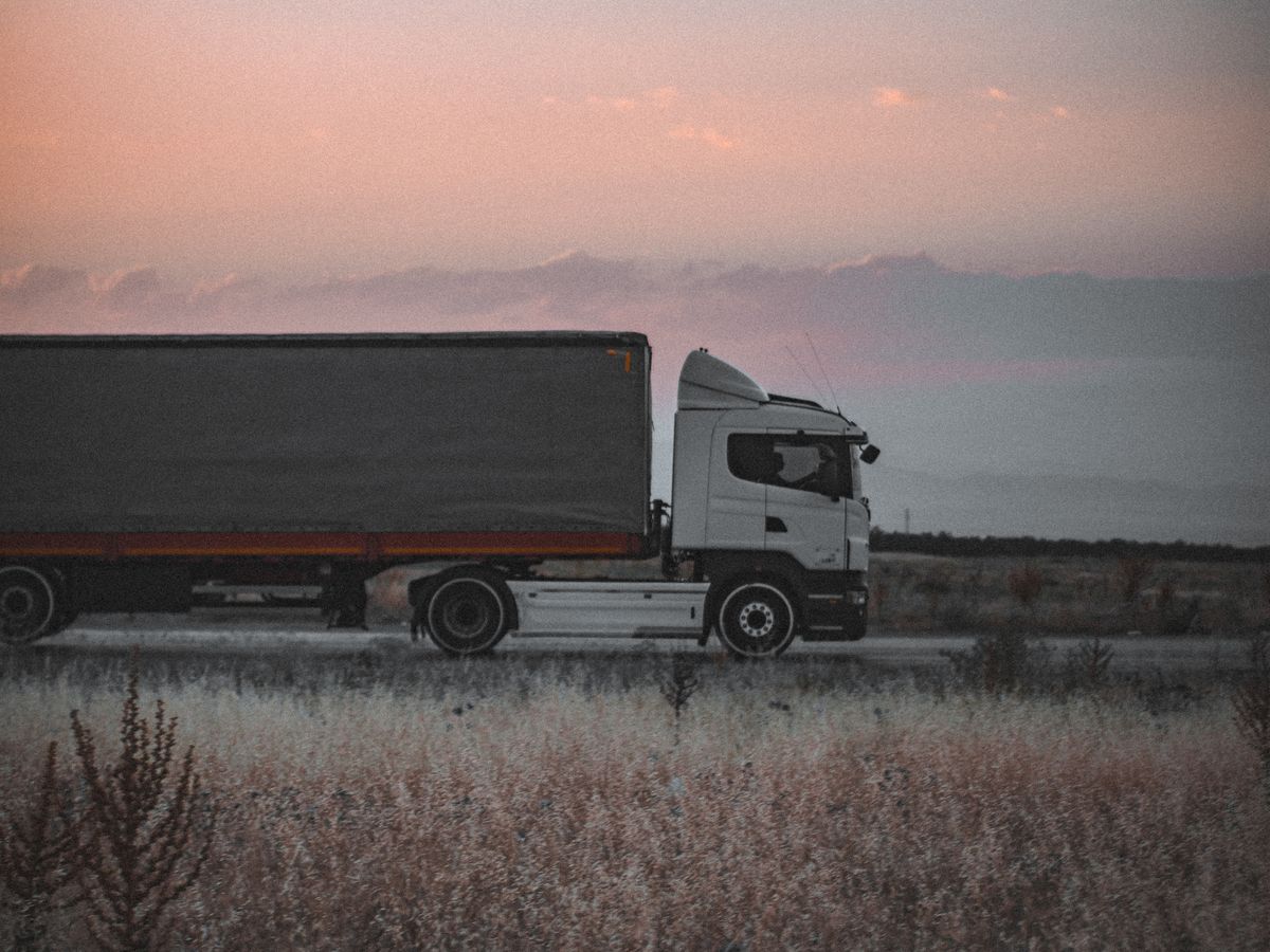 Articulated lorry with a curtain-sided trailer travelling along an open road at dusk