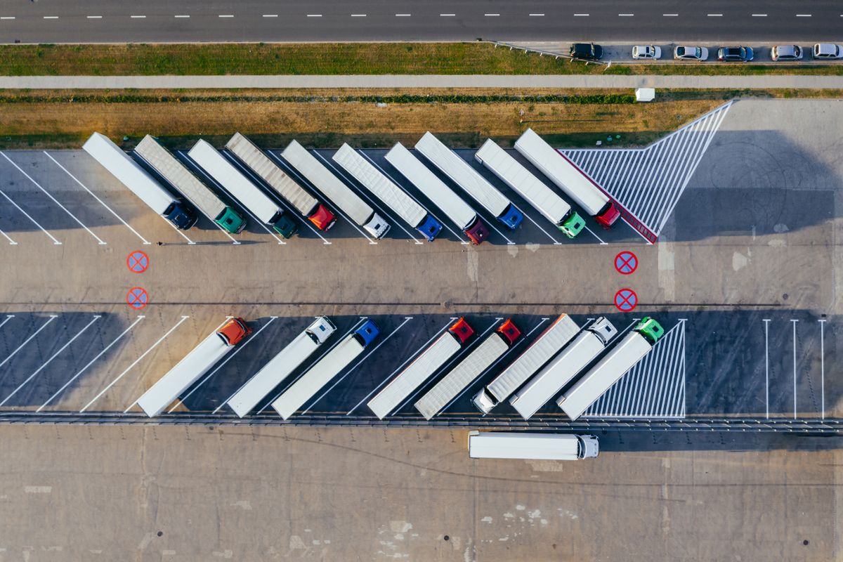 Aerial view of articulated lorries parked in rows at a lorry park beside a main road