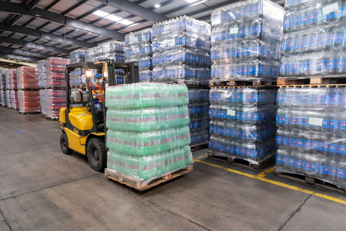 Forklift moving shrink-wrapped pallets of bottled goods through a warehouse
