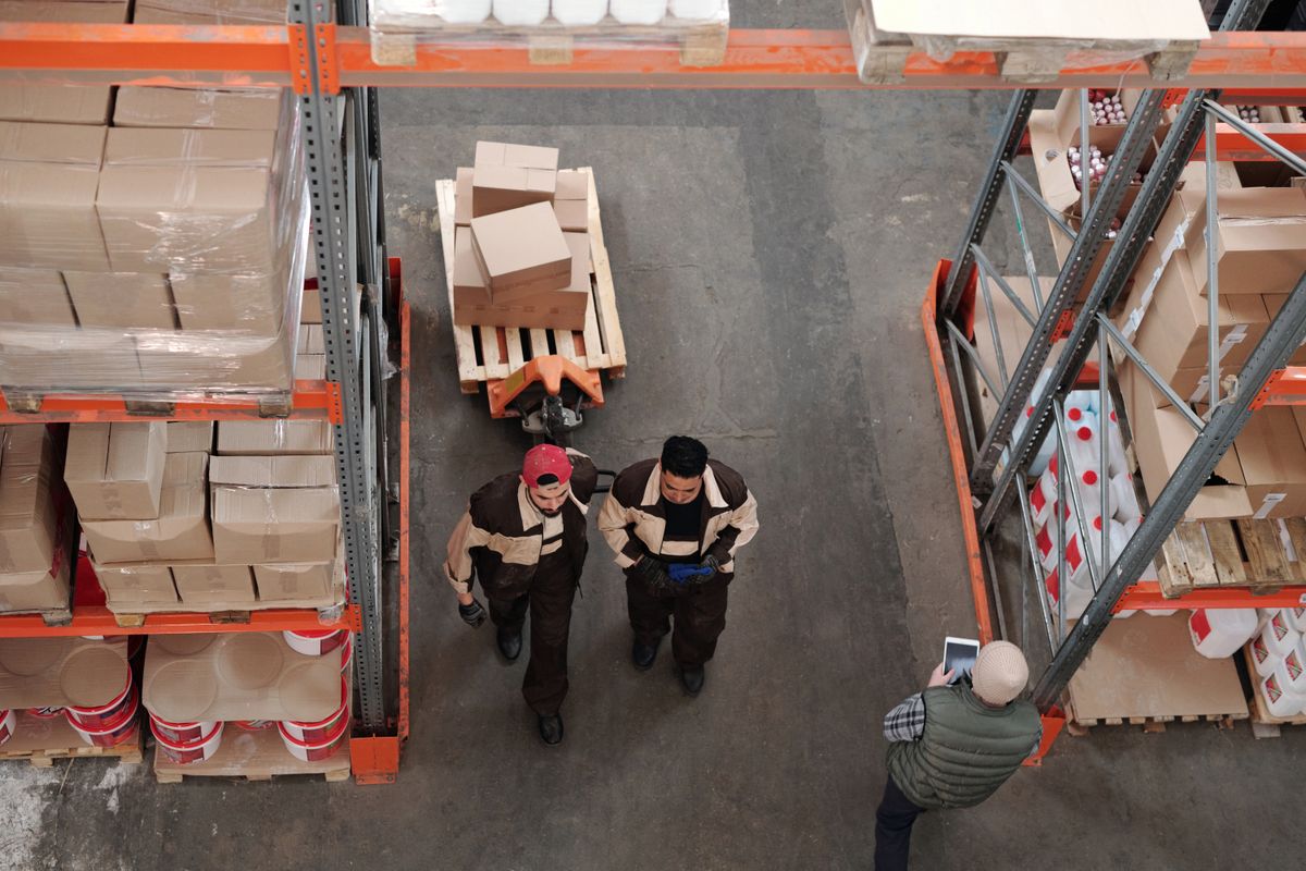Two warehouse workers walking between racking stacked with boxed stock, seen from above